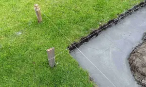 Wyznaczanie fundamentów domu. Naciągnięte sznurki wyznaczają linię wykopu pod uziemienie domu, obok świeżo wylany beton.