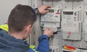 Technik w kamizelce wykonuje wymianę licznika Tauron. Widać nowe liczniki i narzędzia.