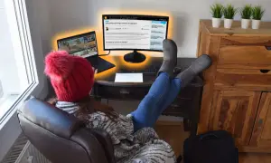 Osoba w czerwonej czapce z pomponem uczy się, jak podłączyć dwa monitory do laptopa, korzystając z artykułu na ekranie.