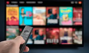 Dłoń trzymająca pilot do telewizora, ekran wyświetla menu z filmami. Dowiedz się, jak wyłączyć napisy w telewizorze.