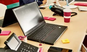 Biurko z laptopem, telefonem i kubkiem. Dowiedz się, jak połączyć telefon z laptopem, aby praca była efektywniejsza.