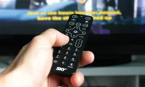 Dłoń trzyma pilot, by jak wyszukać kanały w telewizorze. Widoczne przyciski MENU, LISTA i CH.
