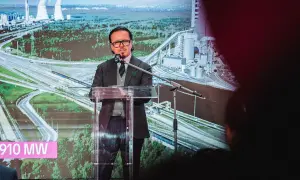 Mężczyzna przemawia na tle wizualizacji elektrowni i autostrady. Na ekranie widnieje napis "910 MW", symbolizujący zwiększenie mocy przyłączeniowej Tauron.