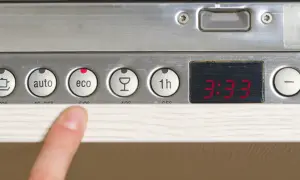 Palec wskazuje przycisk "eco" na panelu zmywarki Whirlpool 6th Sense. Widoczne programy: auto, eco, kieliszek, 1h.