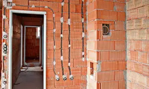 Instalacja elektryczna bezpuszkowa w budowie. Widoczne przewody i puszki instalacyjne w ścianach z cegły.