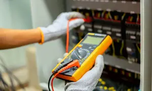 Elektryk sprawdza instalację, by ustalić, ile kosztuje przegląd instalacji elektrycznej. Używa multimetru do pomiarów.