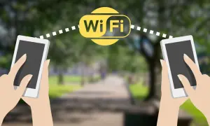 Dwie dłonie trzymają telefony, między którymi widoczny jest symbol Wi-Fi. Połączenie wifi direct umożliwia szybką wymianę danych.