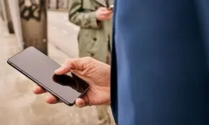 Mężczyzna trzyma smartfon, zastanawiając się, jak skonfigurować telefon. W tle druga osoba również korzysta z telefonu.