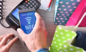 Płatność zbliżeniowa telefonem z funkcją NFC. Transakcja w toku, obok kolorowe torby na zakupy.