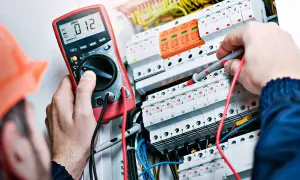 Elektryk z uprawnieniami SEP do 1kV sprawdza instalację elektryczną multimetrem.