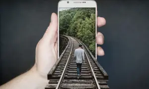 Dłoń trzyma telefon z ekranem **amoled**, na którym widać mężczyznę idącego po torach kolejowych przez las.