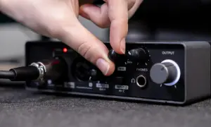 Dłoń obraca pokrętło MIX na panelu miksera audio. Widoczne wejście aux i inne złącza.