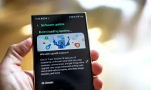 Dłoń trzyma smartfon z ekranem aktualizacji oprogramowania "Downloading update..." z grafiką Galaxy AI.