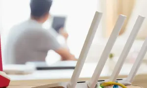 Konfiguracja routera Wi-Fi z widocznym żółtym kablem Ethernet. W tle osoba korzystająca z tabletu.