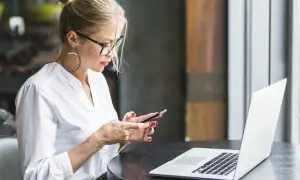 Kobieta w okularach i białej koszuli korzysta z telefonu, obok leży laptop. Upewnij się, że Twoje datezone połączenie nie jest prywatne.