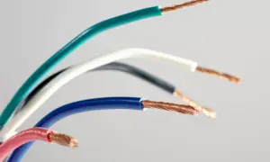Pięć przewodów elektrycznych w różnych kolorach: zielonym, białym, czarnym, niebieskim i różowym, odsłaniających miedziane żyły. Różnorodność kolorów faz ułatwia identyfikację.