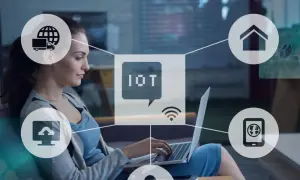 Kobieta pracuje przy laptopie, otoczona ikonami symbolizującymi internet rzeczy (IoT): dom, chmura, ciężarówka, smartfon.