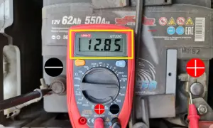 Jak sprawdzić akumulator miernikiem? Wynik 12.85V wskazuje na dobry stan baterii. Czerwona sonda na plusie, czarna na minusie.