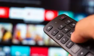 Dłoń trzyma pilot, a na ekranie telewizora widać kolorowe kafelki z filmami. Zastanawiasz się, iptv co to? To przyszłość telewizji!