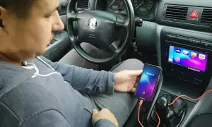 Mężczyzna w samochodzie pokazuje, jak połączyć telefon z autem za pomocą kabla i aplikacji Weblink.
