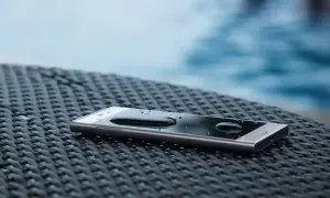 Smartfon z kroplami wody na ekranie, leżący na plecionej powierzchni. IP68 co oznacza? Ochronę przed zanurzeniem w wodzie.