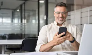 Uśmiechnięty mężczyzna z telefonem w dłoni, szukający informacji, jak udostępnić internet z telefonu na laptopa.