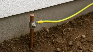 Uziemienie w starej instalacji: miedziany pręt w ziemi z żółto-zielonym przewodem.