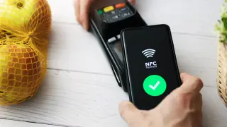 Szybkie zakupy jabłek dzięki płatnościom bezdotykowym NFC. Telefon zbliżony do terminala, zielony znaczek potwierdza transakcję.