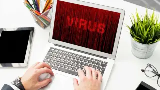 Ręce na klawiaturze laptopa, na ekranie napis "VIRUS". Czas dowiedzieć się, jak usunąć wirusa z komputera.