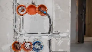 Rozpoczynająca się instalacja elektryczna w domu: widoczne puszki instalacyjne z przewodami, rurki ochronne i kable.