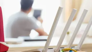 Konfiguracja routera Wi-Fi z widocznym żółtym kablem Ethernet. W tle osoba korzystająca z tabletu.