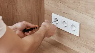 Ręce majsterkowicza dokręcają śrubę w białym gniazdku, zapewniając bezpieczne napięcie w gniazdku.