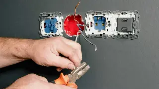 Instalator pokazuje, jak podłączyć gniazdko, przygotowując przewody do montażu.