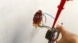 Instalator podłącza włącznik światła do puszki, używając śrubokręta. Widać przewody elektryczne wychodzące ze ściany.