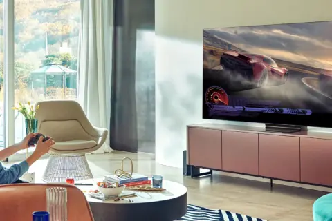 Młody mężczyzna gra w wyścigi na telewizorze 65 cali. Idealna odległość od telewizora 65 cali zapewnia immersję w grze.