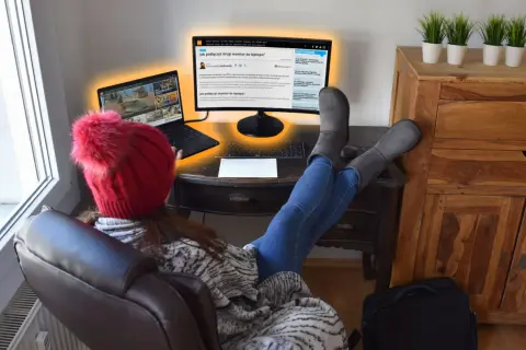 Osoba w czerwonej czapce z pomponem uczy się, jak podłączyć dwa monitory do laptopa, korzystając z artykułu na ekranie.