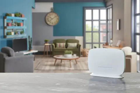 Biały router na blacie, w tle salon z kanapami i zegarem. Zastanawiasz się qos co to? To jakość usług, kluczowa dla płynnego internetu.