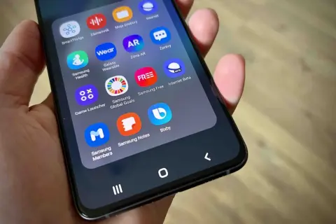Na ekranie telefonu widać ikony aplikacji, w tym Bixby, Samsung Health, Galaxy Wearable i Game Launcher.