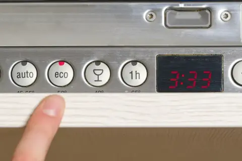 Palec wskazuje przycisk "eco" na panelu zmywarki Whirlpool 6th Sense. Widoczne programy: auto, eco, kieliszek, 1h.