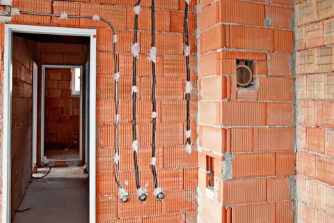 Instalacja elektryczna bezpuszkowa w budowie. Widoczne przewody i puszki instalacyjne w ścianach z cegły.