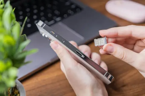 Ręka trzyma duplikat karty SIM obok telefonu.