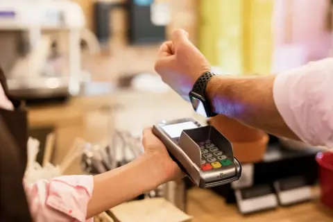 Klient płaci zbliżeniowo zegarkiem z technologią nfc przy terminalu płatniczym.