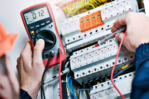 Elektryk z uprawnieniami SEP do 1kV sprawdza instalację elektryczną multimetrem.