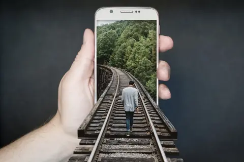 Dłoń trzyma telefon z ekranem **amoled**, na którym widać mężczyznę idącego po torach kolejowych przez las.