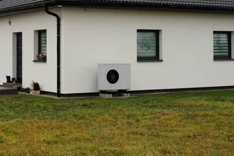 Nowoczesna pompa ciepła przy białym domu. Idealna do ogrzania domu 150m2, zapewnia komfort i oszczędność.