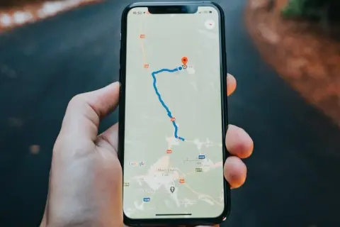 Dłoń trzyma iPhone'a z mapą Google, pokazującą trasę i lokalizację.