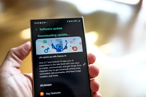 Dłoń trzyma smartfon z ekranem aktualizacji oprogramowania "Downloading update..." z grafiką Galaxy AI.