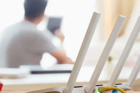 Konfiguracja routera Wi-Fi z widocznym żółtym kablem Ethernet. W tle osoba korzystająca z tabletu.