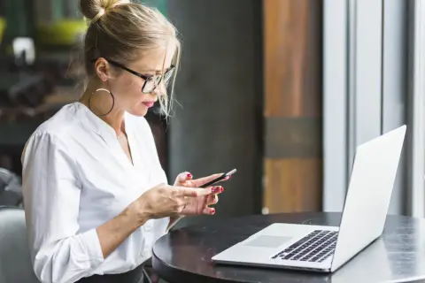 Kobieta w okularach i białej koszuli korzysta z telefonu, obok leży laptop. Upewnij się, że Twoje datezone połączenie nie jest prywatne.