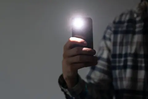 Dłoń trzyma smartfon z włączoną latarką. Dowiedz się, jak wyłączyć latarkę w telefonie, aby oszczędzać baterię.
